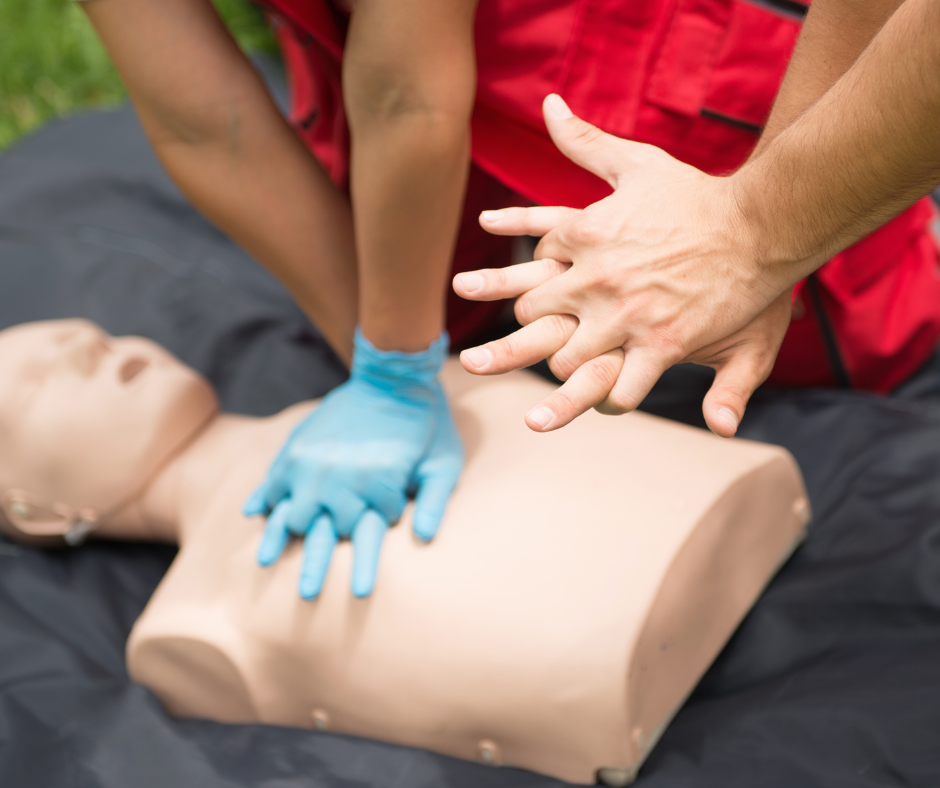 One person practicing CPR chest compressions on a dummy while another person shows the proper hand placement.